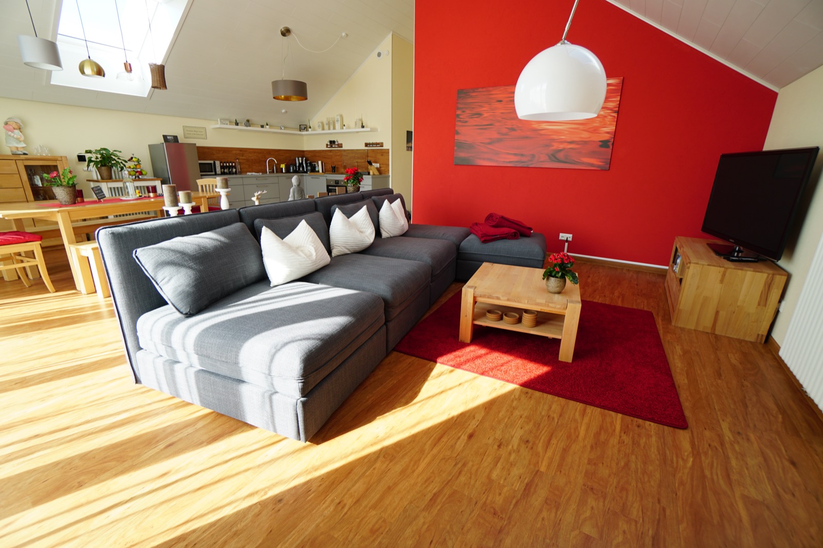 Wohnbereich mit großer Couch vor der roten Wand, Couchtisch aus Holz und Fernseher
